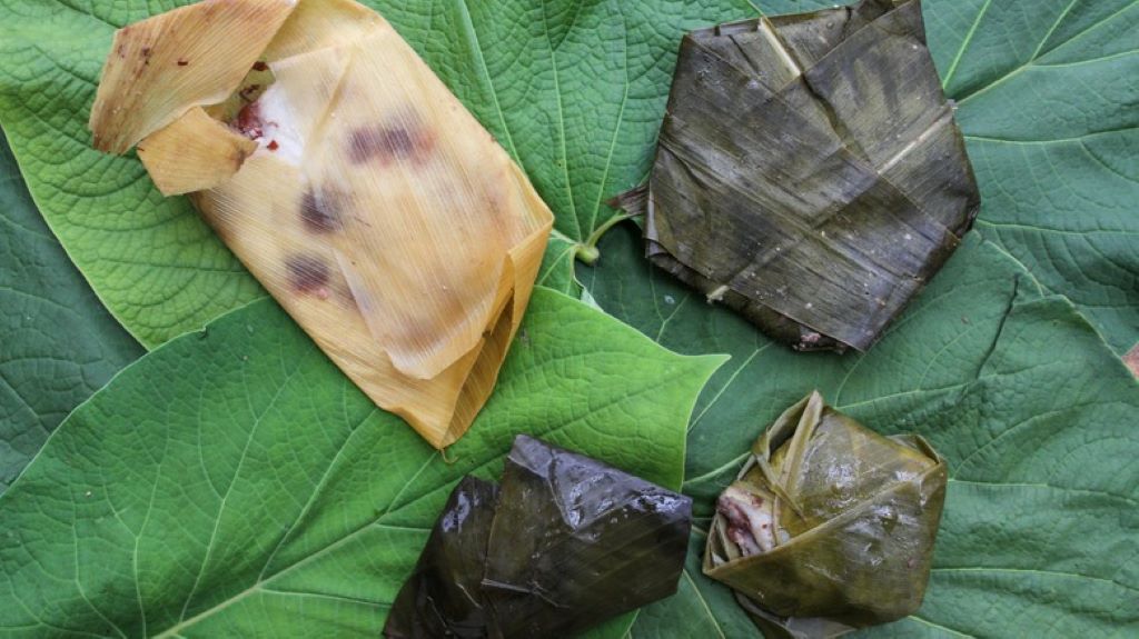 A large, fresh, heart-shaped green hoja santa leaf resting on a wooden table, one of the essential rare spices for mole