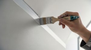 Close-up of a hand using an angled brush to cut in a sharp paint line along a white ceiling