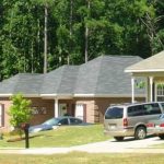 First-time home buyers standing in front of a new Alabama suburban house with mortgage approval documents