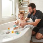 A man kneeling on a plush gray bath mat next to a bathtub.