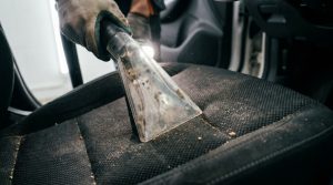 Person cleaning car seats using a compact vacuum attachment.