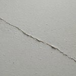 Extreme close view of a thin hairline crack across a painted basement wall