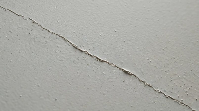 Extreme close view of a thin hairline crack across a painted basement wall